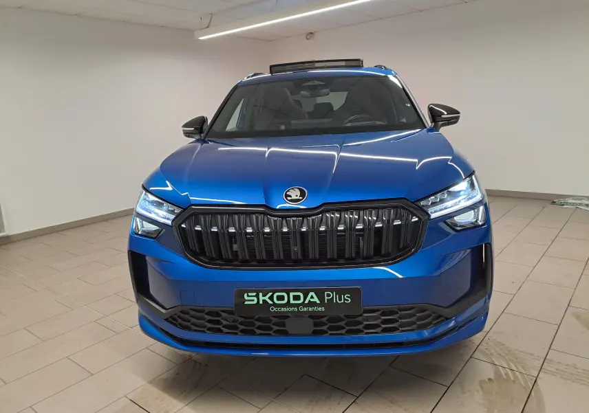 Vue avant d'un Skoda Kodiaq Bleu RS 2025 avec calandre noire et phares LED allumés dans un intérieur neutre.