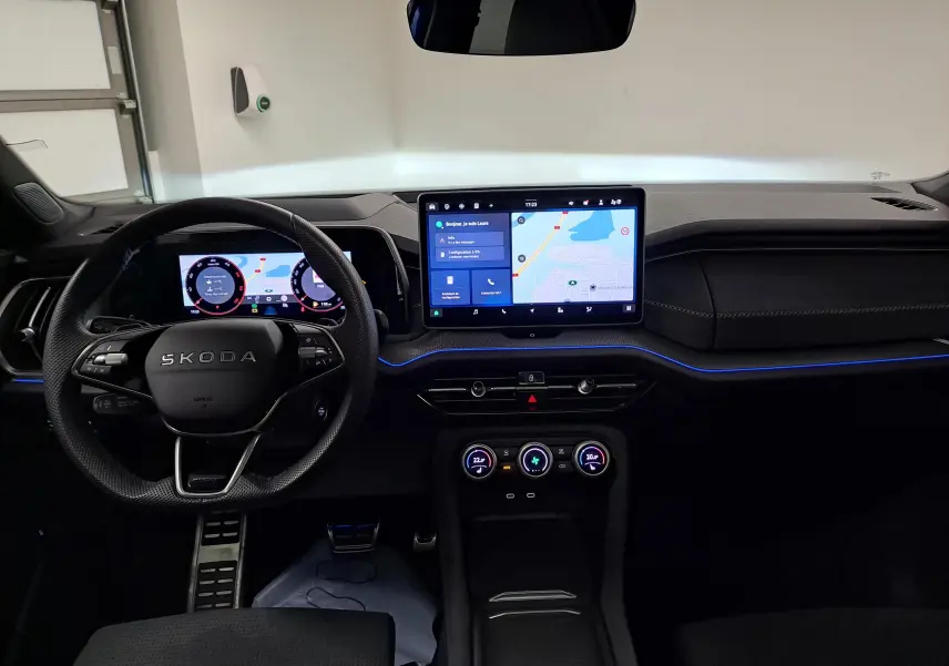 Vue intérieure frontale du tableau de bord du Skoda Kodiaq 2025 avec écran tactile central et éclairage d'ambiance bleu.