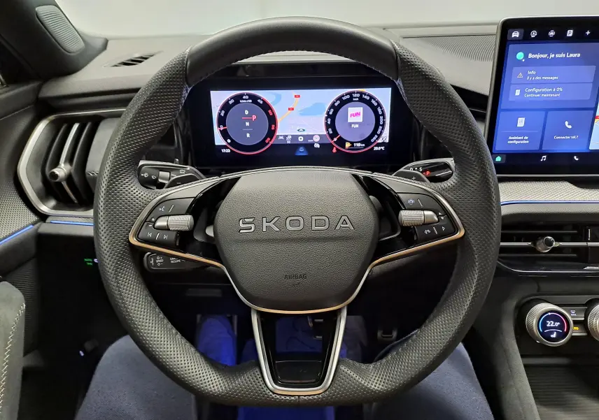 Vue intérieure centrée sur le volant perforé SKODA avec tableau de bord numérique et écran tactile à droite.
