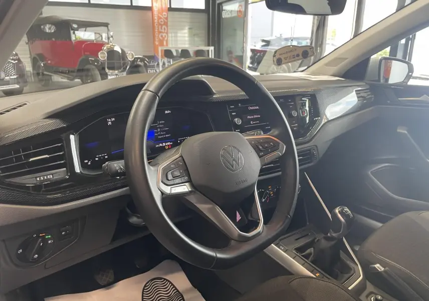 Vue intérieure du poste de conduite d'une Volkswagen Polo gris clair 2024, volant cuir multifonction et levier de vitesses manuel.