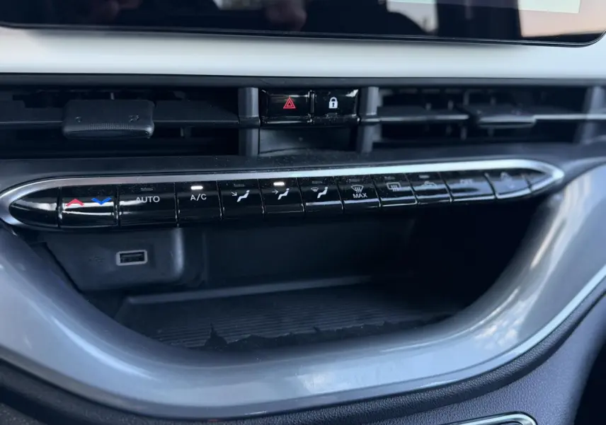 Gros plan sur la console centrale noire de la Fiat 500 électrique blanche, avec commandes de climatisation et prises USB visibles.