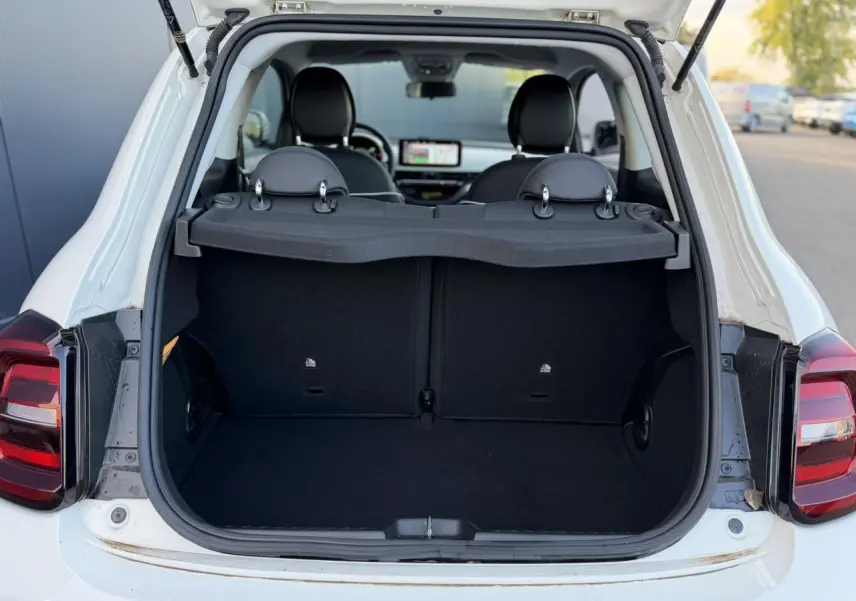 Coffre ouvert vu de l'arrière d'une Fiat 500 électrique blanc Arctic, banquette arrière et intérieur noir visibles.