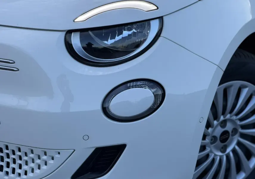 Gros plan sur le phare avant gauche blanc Artic de la FIAT 500 électrique 2024 avec jante alliage visible.