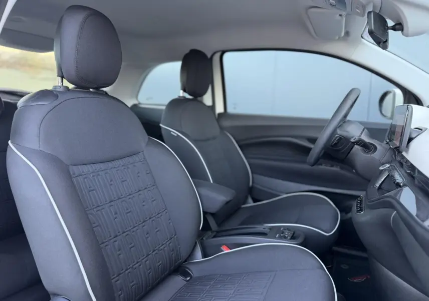 Vue intérieure côté droit de la Fiat 500 électrique 2024 avec sièges tissu noir Seaqual et accoudoir central.
