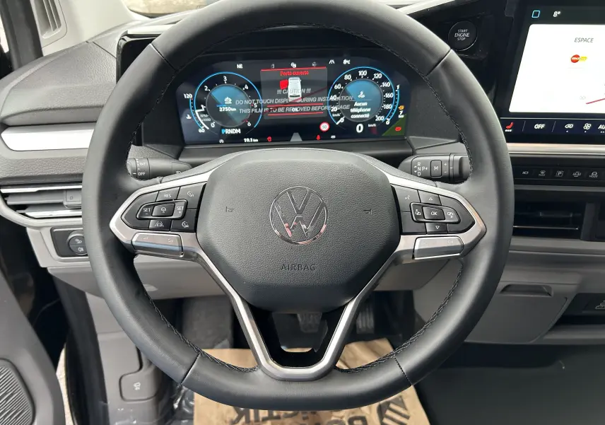 Vue rapprochée du volant multifonction noir du Volkswagen Transporter T7 avec tableau de bord digital et écran tactile.