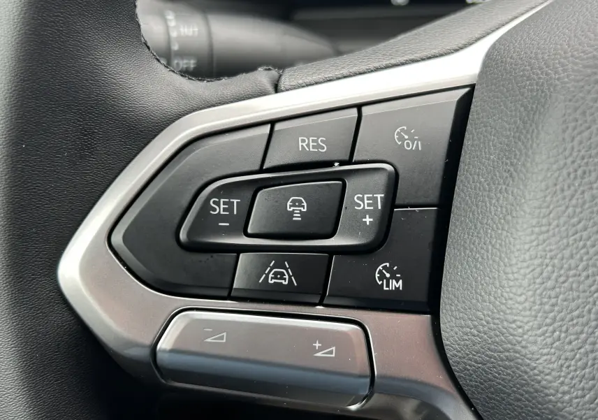 Gros plan sur les commandes de régulateur de vitesse au volant en cuir noir du Volkswagen Transporter T7 Business.