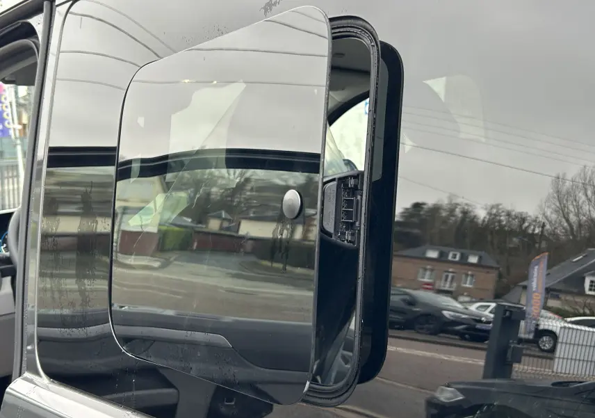 Rétroviseur extérieur gauche du Volkswagen Transporter T7 ProCab graphite dust, avec reflet de la route et des bâtiments alentours.