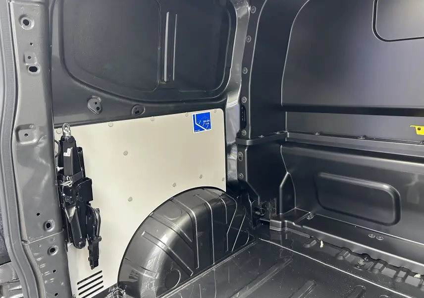Détail intérieur du coffre côté gauche du Volkswagen Transporter T7 ProCab Graphite Dust, montrant la cloison et la roue de secours.