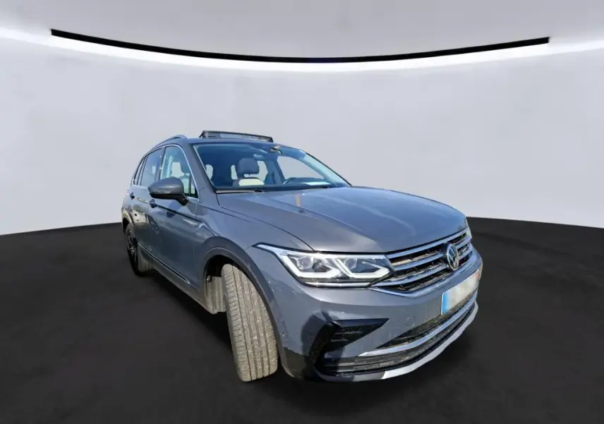 Volkswagen Tiguan gris 3/4 avant droit avec toit ouvrant panoramique visible sur fond neutre.