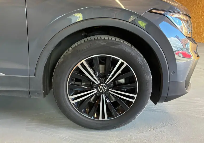 Gros plan sur la roue avant droite d’un Volkswagen Tiguan gris, mettant en valeur la jante noire et argentée.