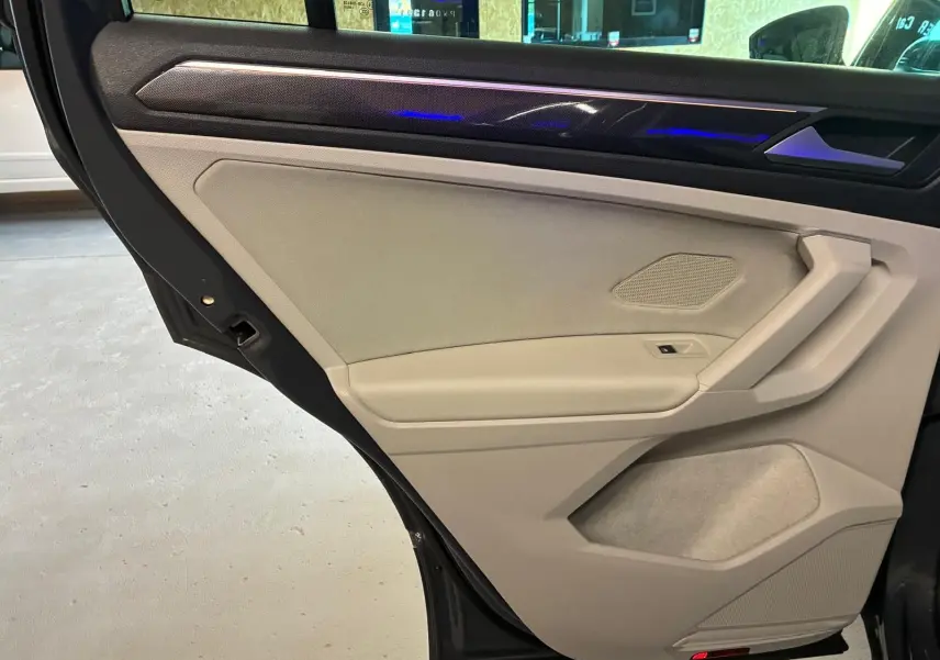 Gros plan sur la porte arrière gauche beige du Volkswagen Tiguan 2023 avec éclairage d'ambiance bleu et habillage textile.