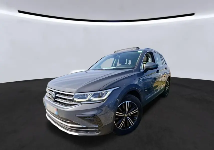 Volkswagen Tiguan gris 3/4 avant droit avec toit ouvrant et jantes noires sur fond neutre.