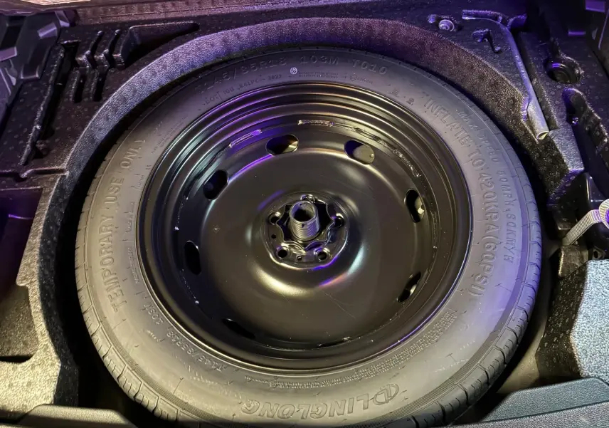 Gros plan sur la roue de secours noire dans le coffre du Volkswagen Tiguan gris 2023, détail du pneu temporaire.