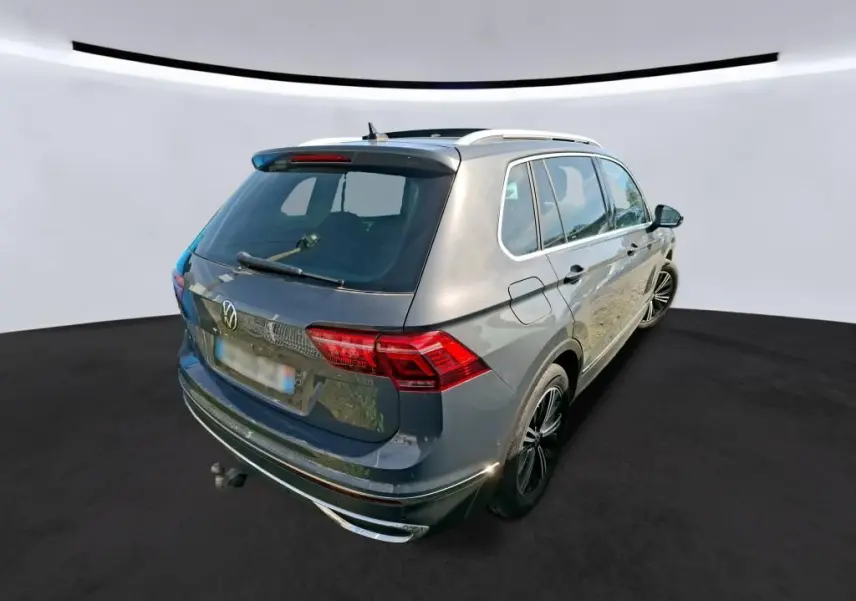Volkswagen Tiguan gris 3/4 arrière droit avec toit ouvrant panoramique et attelage visible sur fond neutre.
