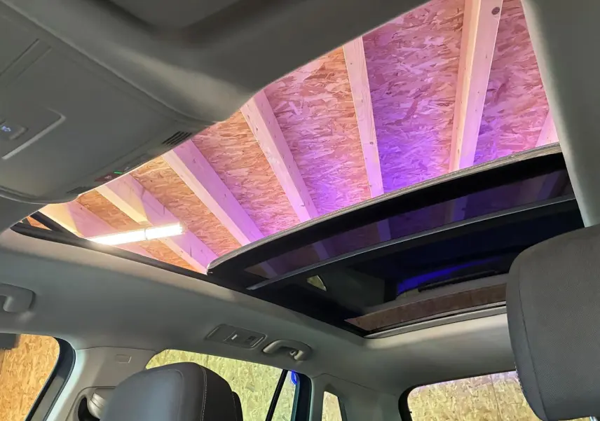 Vue intérieure du toit ouvrant panoramique ouvert du Volkswagen Tiguan gris 2023, avec ciel de toit clair et siège avant visible.