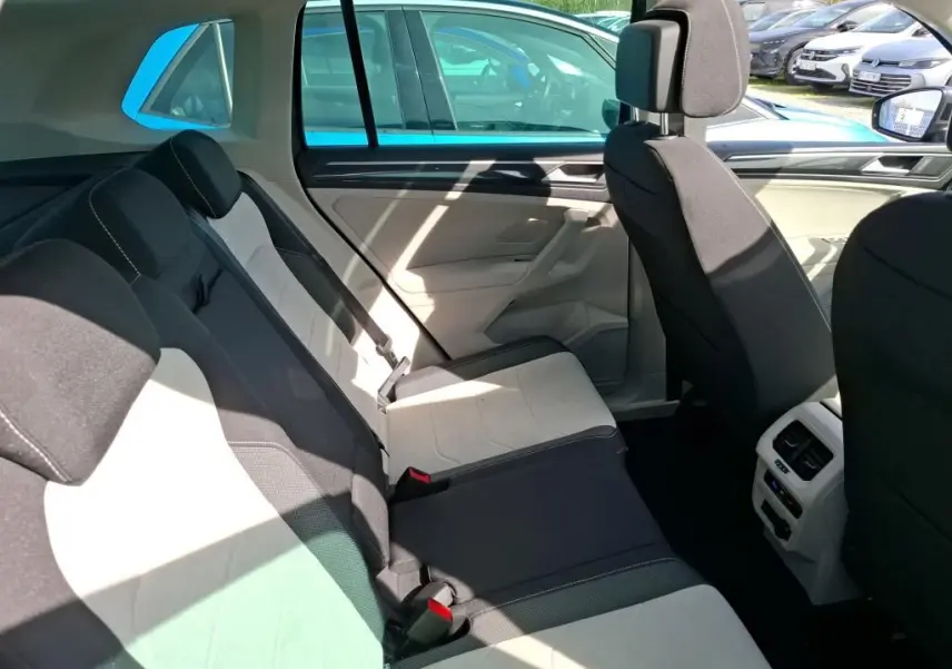 Vue latérale intérieure du siège arrière du Volkswagen Tiguan 2023 gris, montrant les sièges bicolores et la console centrale arrière.