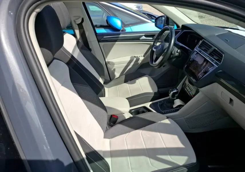 Vue intérieure côté conducteur du Volkswagen Tiguan gris 2023, sièges tissu clair et tableau de bord moderne avec écran tactile.