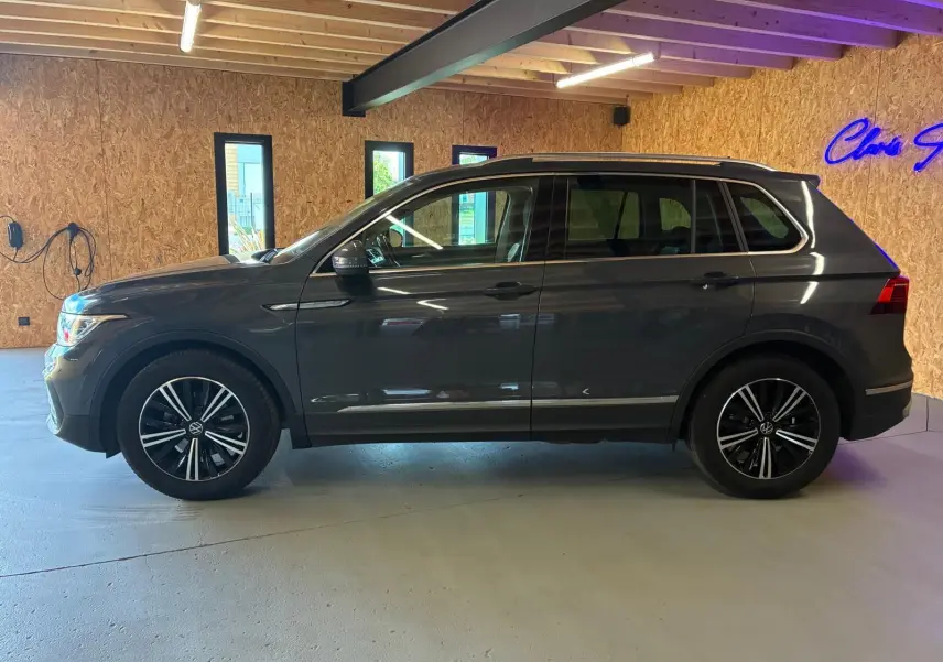 Vue de profil côté gauche d'un Volkswagen Tiguan gris 2023 avec jantes alliage et toit ouvrant panoramique visible.