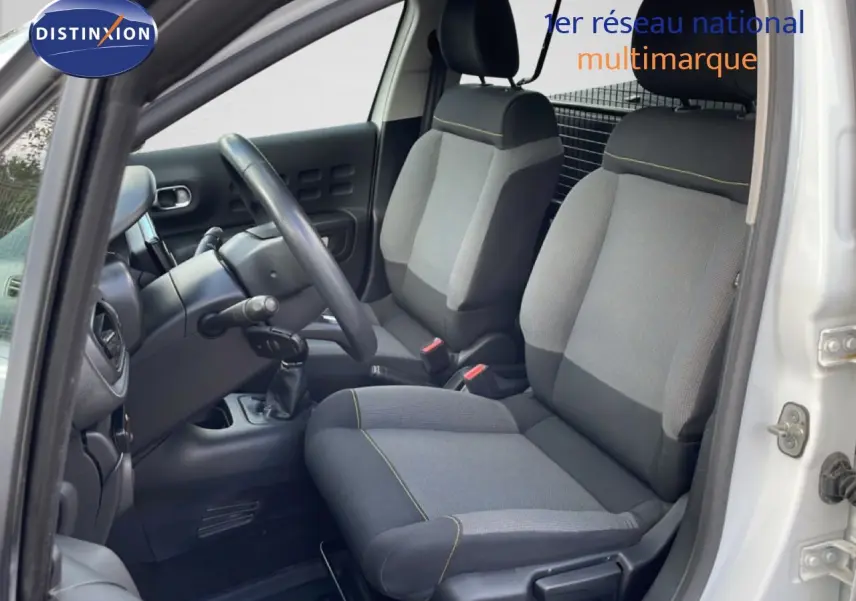 Vue intérieure côté conducteur de la Citroën C3 Société blanche, sièges tissu gris avec surpiqûres jaunes visibles.