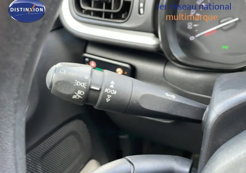 Gros plan sur la commande des phares et clignotants à gauche du volant dans l’habitacle d’une Citroën C3 blanche.