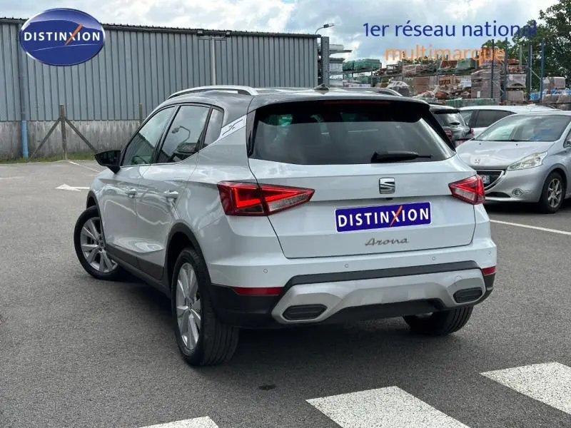 Vue 3/4 arrière droite d’un SEAT Arona blanc Nevada avec toit noir et feux arrière LED en parking.