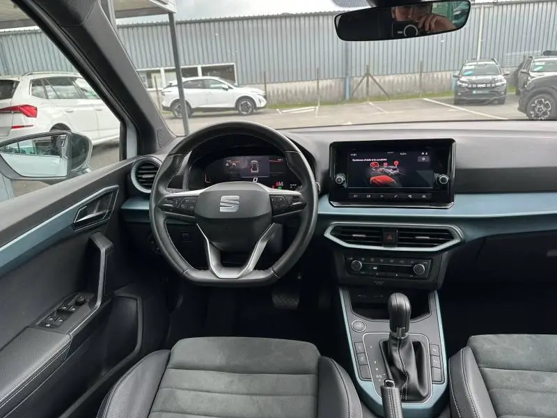 Vue intérieure avant du SEAT Arona 2025 avec tableau de bord noir, volant cuir multifonction et écran tactile central.
