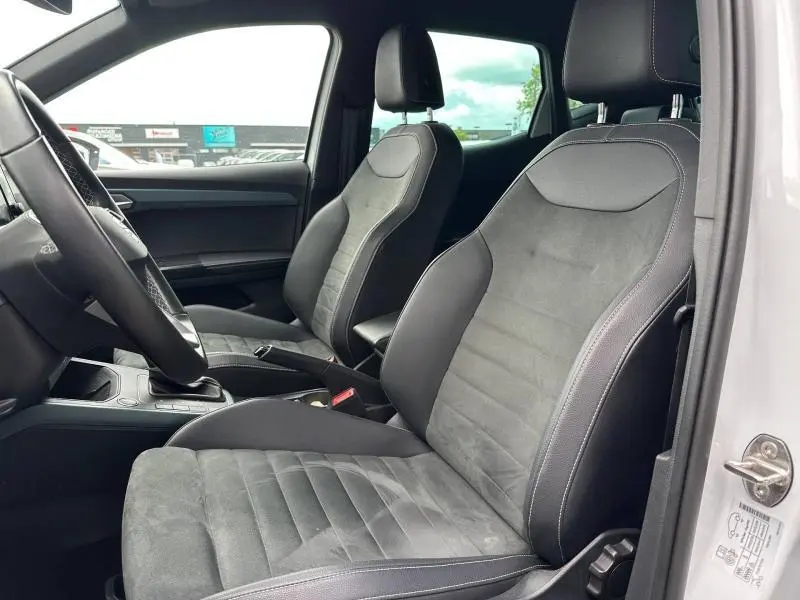 Vue intérieure côté gauche montrant les sièges avant en tissu gris Sano du SEAT Arona 2025 avec porte ouverte blanche.