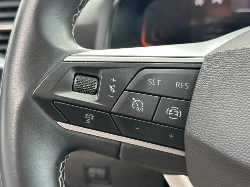Gros plan sur les commandes du volant cuir multifonction du SEAT Arona 2025, côté gauche, avec réglages de vitesse et assistance.