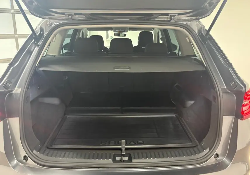 Coffre ouvert vu de l'arrière d'un Skoda Kodiaq gris graphite 2025, avec tapis de coffre marqué KODIAQ.
