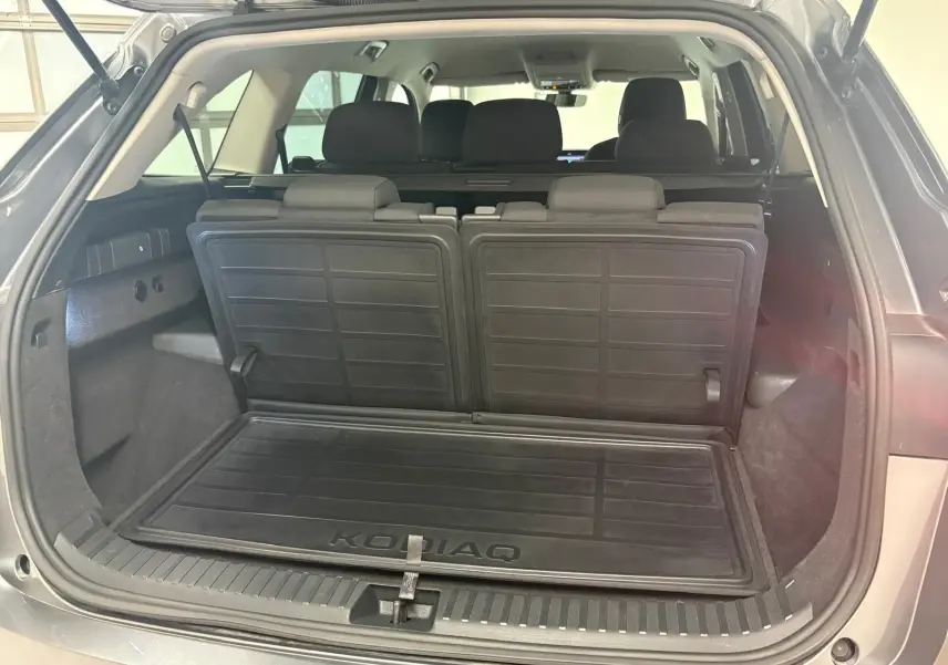 Vue arrière du coffre ouvert du Skoda Kodiaq gris graphite 2025, montrant la banquette rabattue et le tapis de coffre marqué KODIAQ.