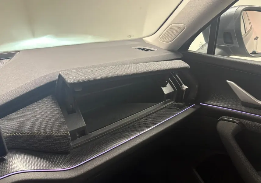 Intérieur du Skoda Kodiaq 2025 côté passager, tableau de bord gris avec boîte à gants ouverte et éclairage d'ambiance violet.