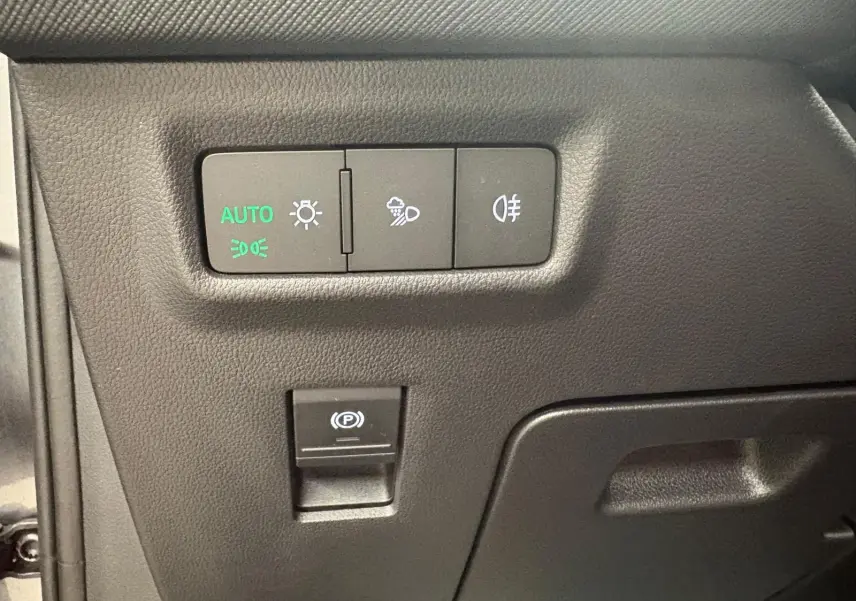 Gros plan sur les commandes d’éclairage et frein de stationnement électrique du Skoda Kodiaq gris graphite, intérieur côté conducteur.