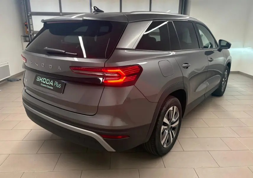 Vue 3/4 arrière droite du Skoda Kodiaq gris graphite 2025 avec feux arrière allumés dans un showroom.