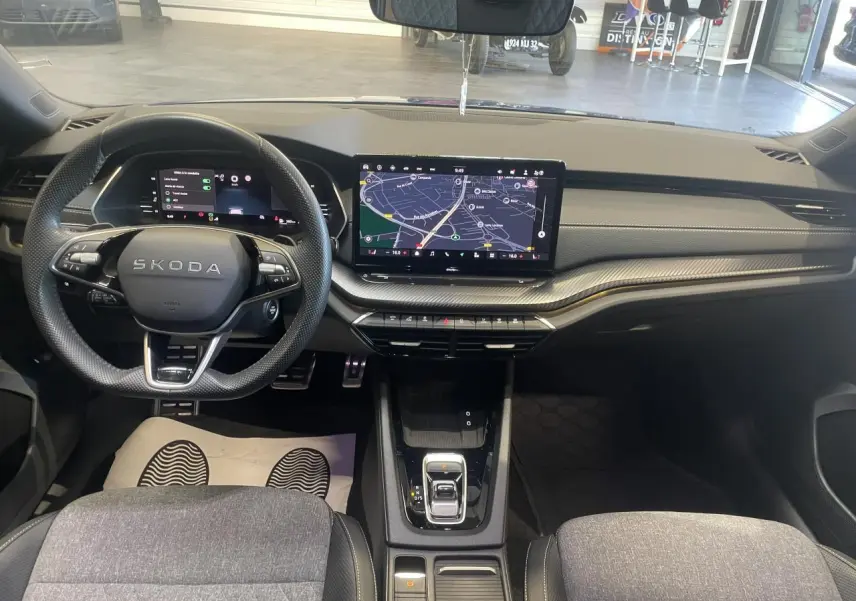Vue intérieure avant de la Skoda Octavia 2025 Sportline, tableau de bord noir avec écran tactile central et volant cuir.