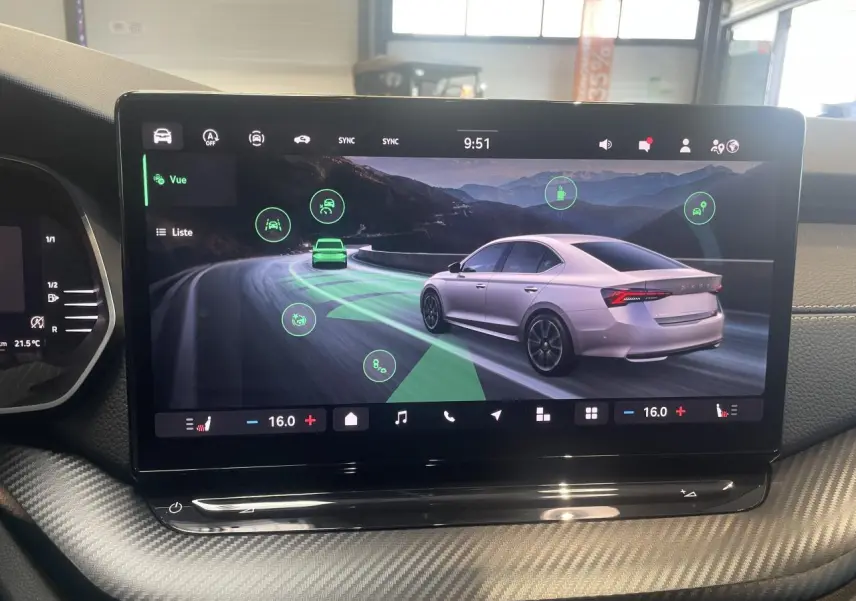 Écran tactile intérieur montrant une Skoda Octavia 2025 gris clair en vue 3/4 arrière sur route sinueuse.
