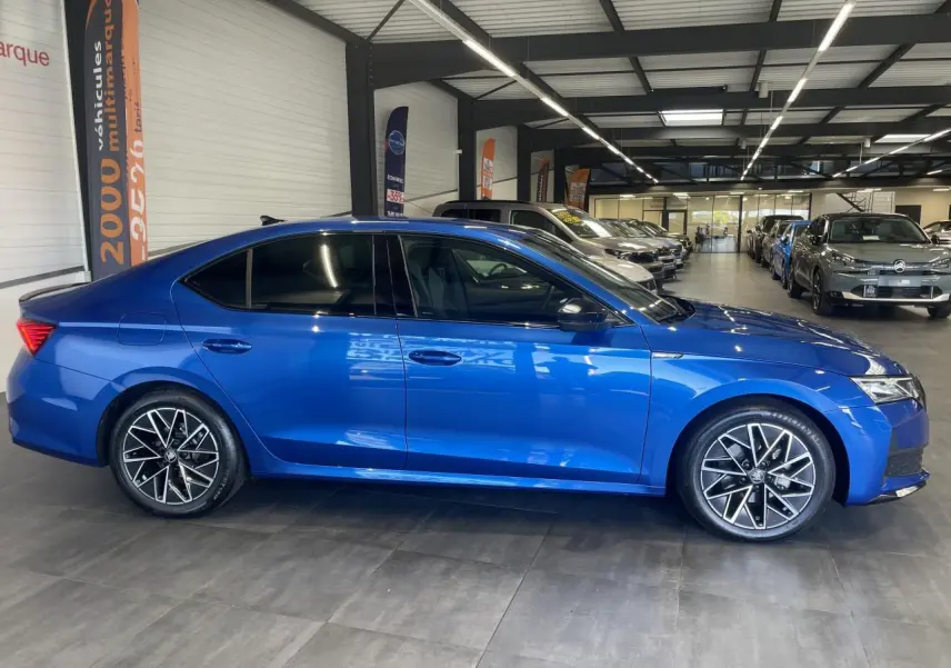 Vue latérale droite d'une Skoda Octavia 2025 bleu foncé avec jantes alliage noires et vitres teintées en showroom.