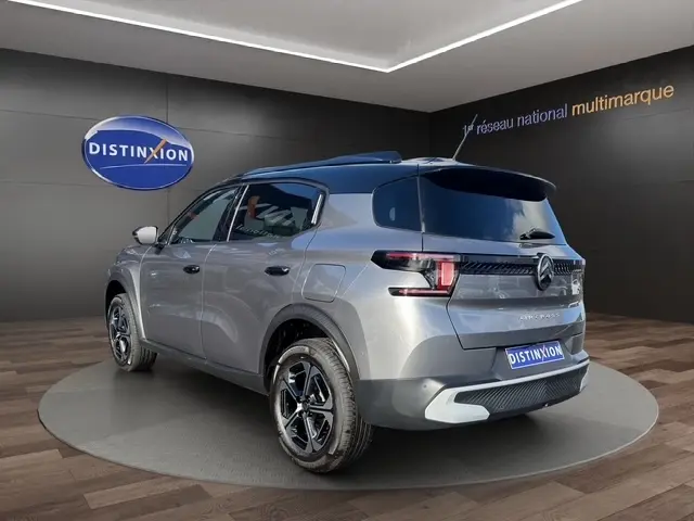 Vue 3/4 arrière droite d'une Citroën C3 Aircross hybride gris foncé avec toit bleu et jantes noires en showroom.