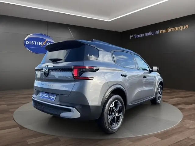 Vue 3/4 arrière droite d'une Citroën C3 Aircross hybride gris foncé avec jantes noires et toit noir en showroom.