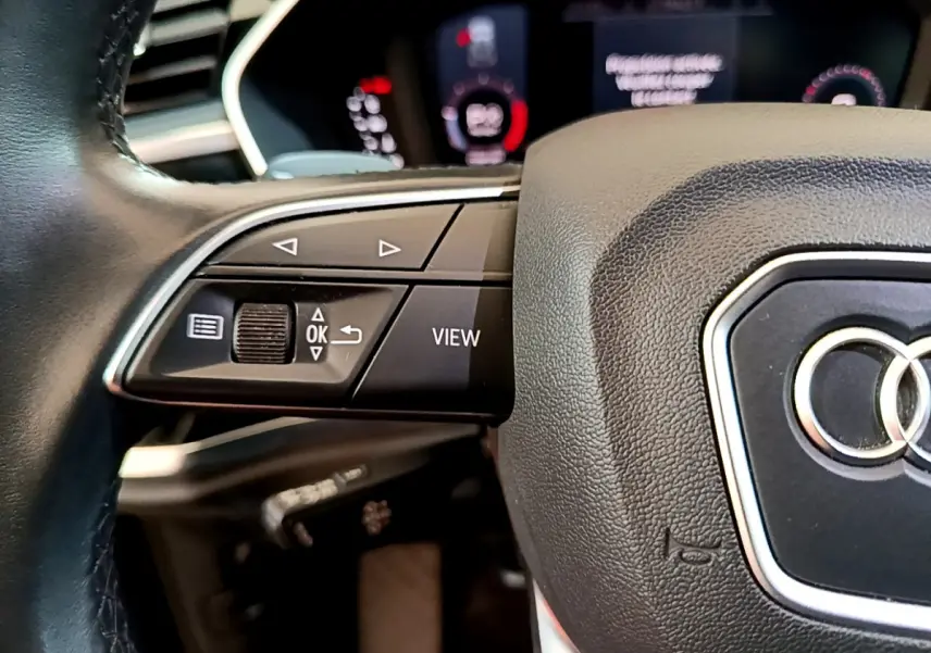 Gros plan sur le volant cuir noir d’un Audi Q3 35 TDI 2021, avec commandes multifonctions et logo Audi central.