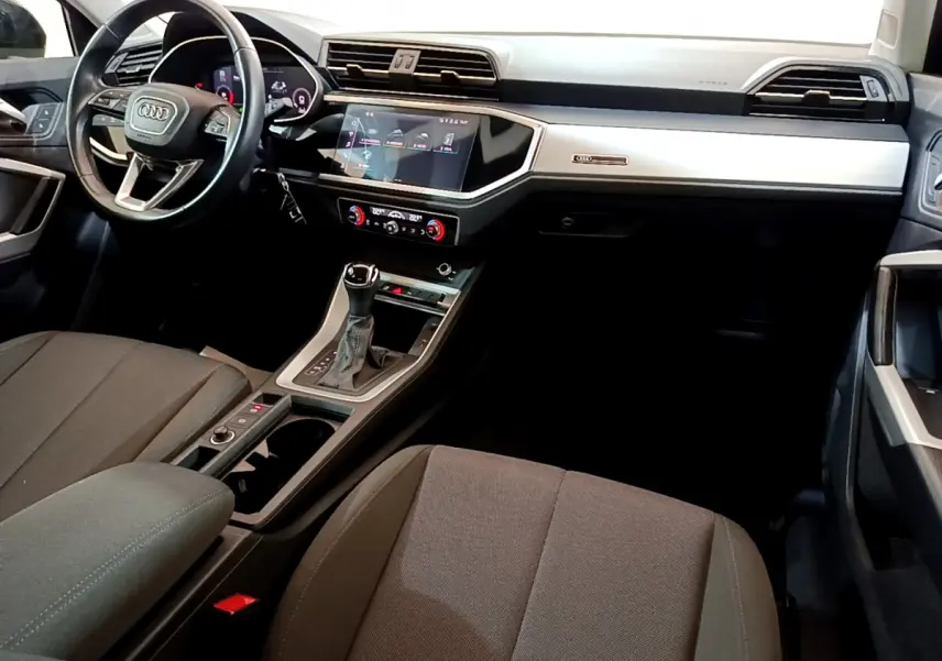 Vue intérieure côté conducteur de l'Audi Q3 35 TDI 2021, tableau de bord moderne avec écran tactile et volant cuir noir.