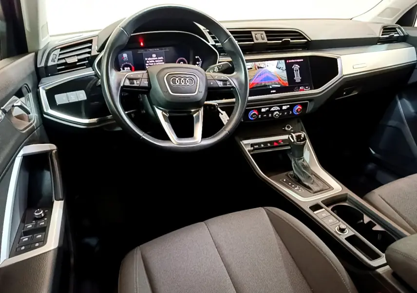 Vue intérieure avant de l'Audi Q3 35 TDI 150 S tronic, tableau de bord noir avec écran tactile et volant cuir multifonctions.