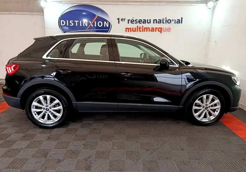 Vue de profil côté gauche d’un Audi Q3 noir 2021 avec jantes alliage et rails de toit chromés en intérieur showroom.
