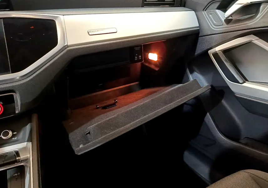 Vue intérieure côté passager de l'Audi Q3 noir 35 TDI 2021 avec boîte à gants ouverte et éclairage intérieur allumé.