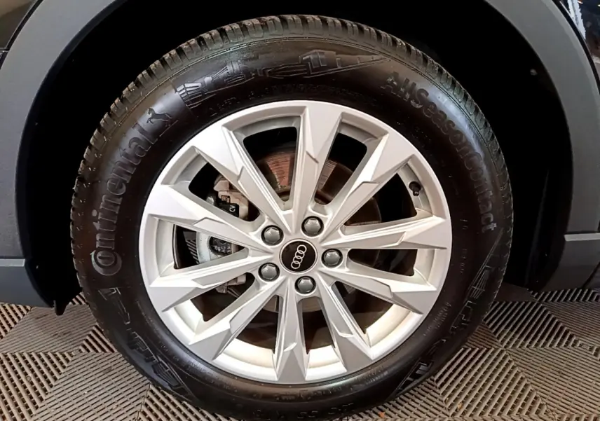 Gros plan sur la roue avant gauche d’un Audi Q3 noir, mettant en valeur la jante alu à design étoilé.