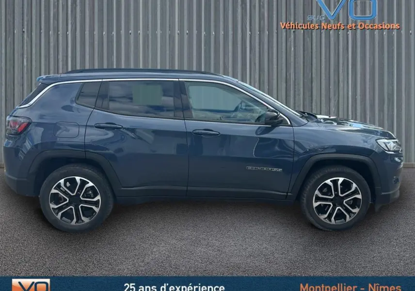 Vue de profil côté gauche d'un Jeep Compass bleu 2023 avec jantes 18 pouces et barres de toit visibles.