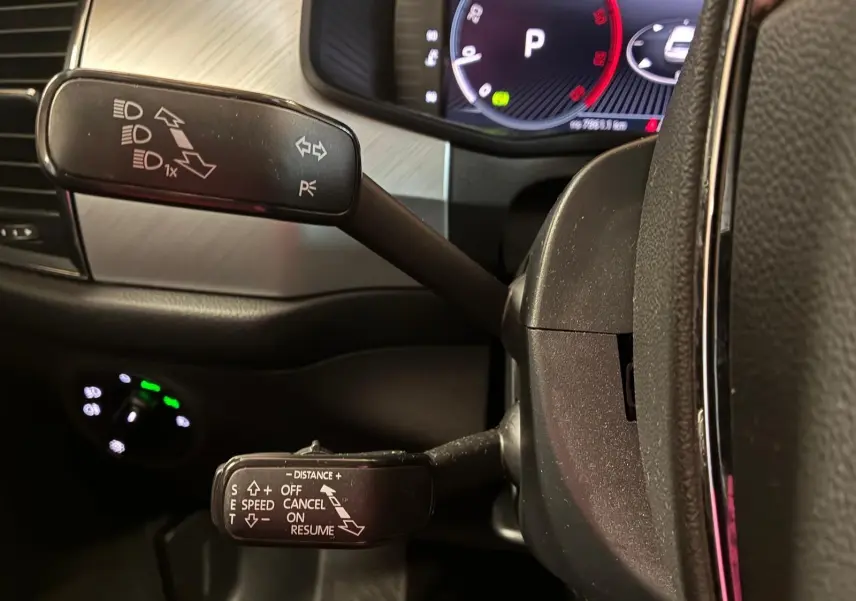 Gros plan sur les commandes au volant d’un Skoda Kodiaq gris, avec tableau de bord numérique en arrière-plan.