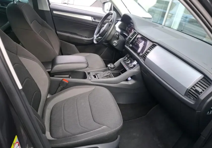 Vue intérieure côté conducteur du Skoda Kodiaq gris 2023, montrant sièges tissu, tableau de bord moderne et console centrale.
