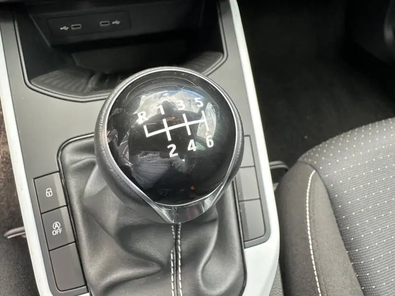 Gros plan sur le levier de vitesse manuel noir brillant de la SEAT Arona 2025, entouré de commandes et tissu gris à pois.