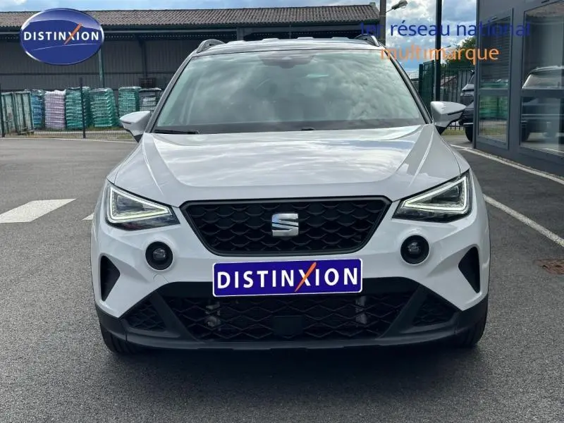 Vue avant d'un SEAT Arona blanc Candy avec toit gris magnétique, calandre noire et feux LED allumés.