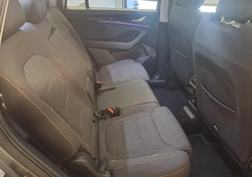 Vue intérieure côté gauche des sièges arrière gris foncé du Skoda Kodiaq 2025 avec éclairage d'ambiance violet sur la porte.